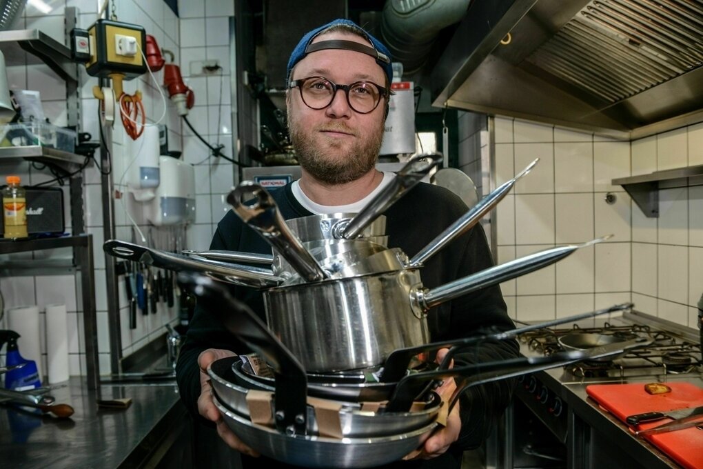 Ein Koch trägt gestapelte Kochtöpfe