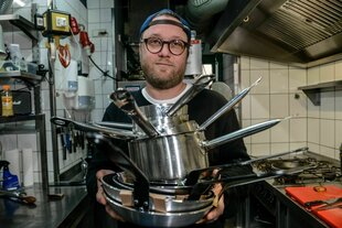 Ein Koch trägt gestapelte Kochtöpfe