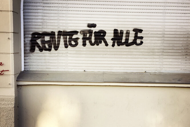 An einem Gebäude steht auf dem angegrauten Rolladen 