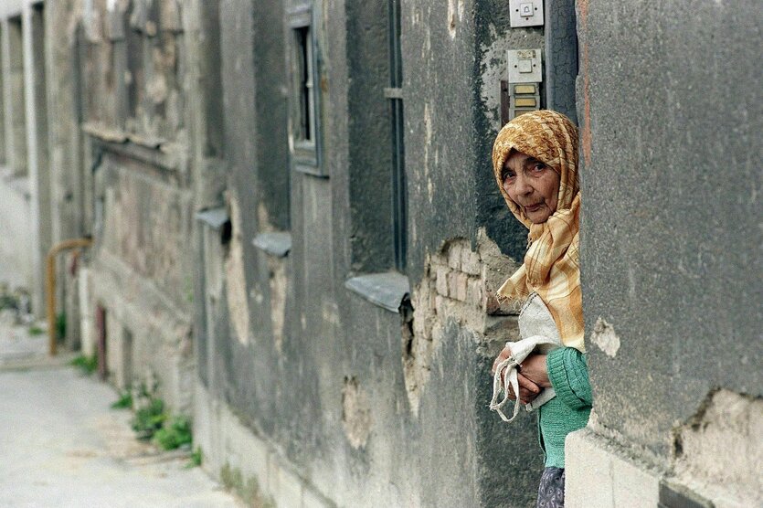 Eine alte Frau mit Kopftuch lugt vorsichtig hinter einem Mauervorsprung