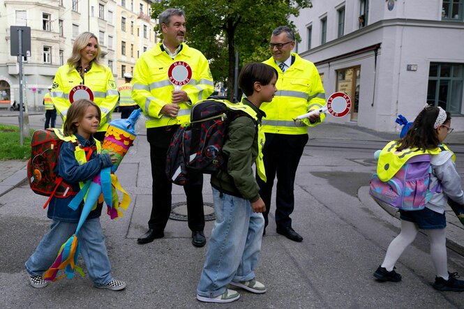 Markus Söder mit anderen Personen als Schülerlotsen mit Kindern auf einer Straße.