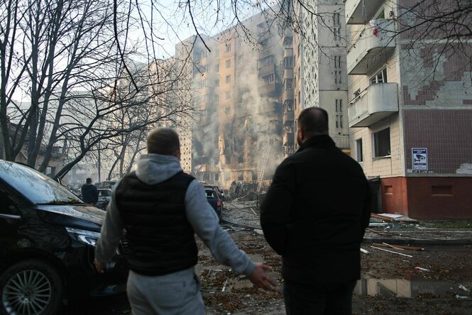 Zwei Personen im Vordergrund, im Hintergrund eine schwer beschädigte Häuserzeile