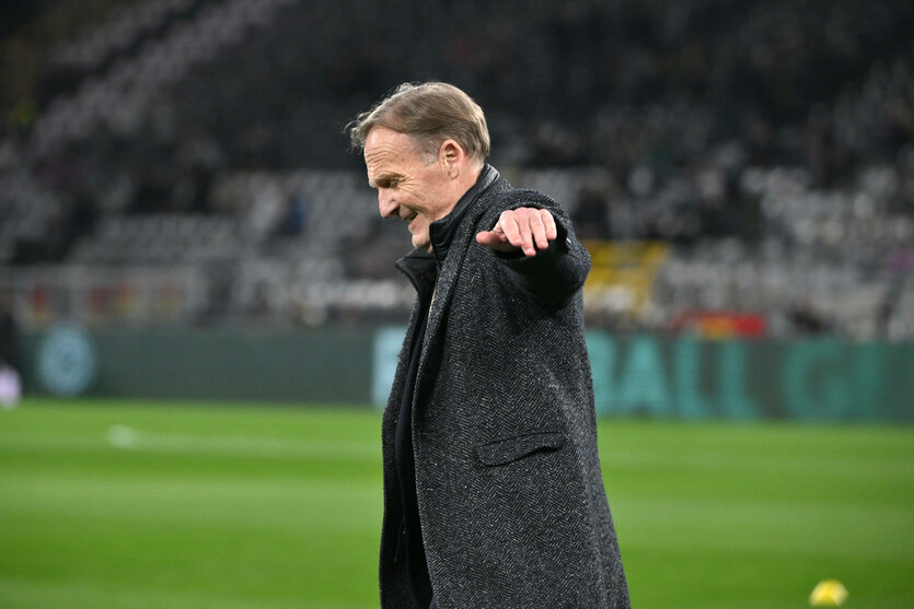Watzke im Mantel breitet auf dem Rasen des Dortmundes Stadions jubelnd beide Arme aus