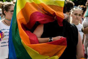 Zwei Personen versteckt unter einer Regenbogen-Fahne