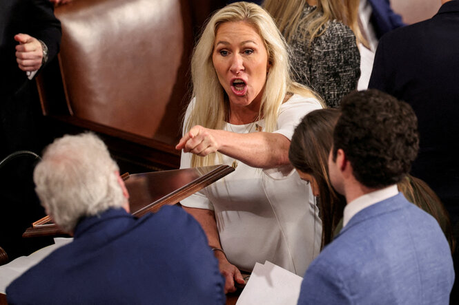 Marjorie Taylor Greene im US-Abgeordnetenhaus. Sie macht einen erbosten Gesichtsausdruck und zeigt mit dem Finger auf einen älteren Parlamentskollegen, der mit dem Rücken zur Kamera sitzt