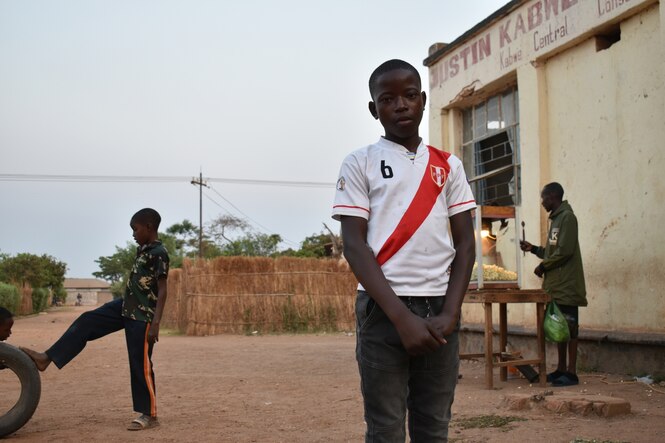 EIn Junge im Fußballtrikot im Vordergrund, dahinter spielen andere Kinder Fußball