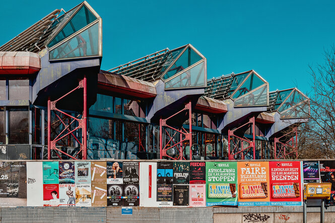 Aussensicht des SEZ in Berlin, das Gebäude steht hinter einer Mauer, die mit bunten Werbeplakaten beklebt ist