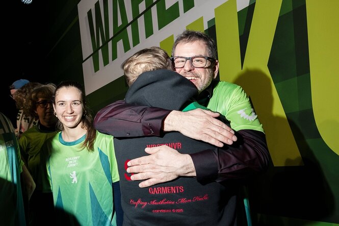 Menschen umarmen sich vor Parteitagskulisse