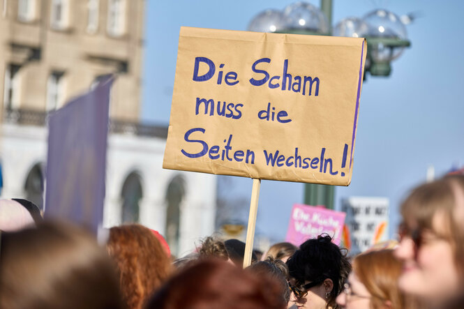 Teilnehmer*innen der Demo am feministischen Kampftag in Hamburg halten ein Schild: „Die Scham muss die Seiten wechseln"
