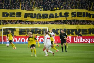 Im Hintergrund große Transparente, auf denen zu lesen ist: Soll das die zukunft des Fußballs sein