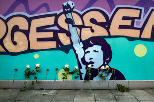 Eine Wand ist mit dem Motiv eines Menschen, der die Faust reckt gestaltet, davor sind weiße Rosen und rote Nelken