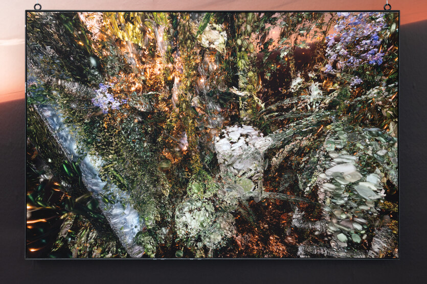 In einem dünnen Stahlrahmen hängt ein Bild von einer wuchernden, organisch wirkenden Struktur in grünlich-weißen und rostroten Farbtönen