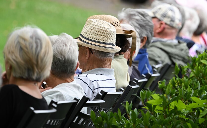 Ältere Menschen sitzen auf einer Bank und man sieht sie von hinten.
