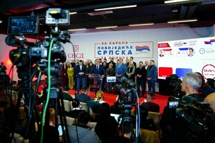 Eine Gruppe steht auf einem Podium, eine Person spricht zu Vertretern der Presse