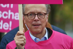Ein Mann mit Brille und pinkem Pulli (Albrecht von der Hagen) hält ein Schild in die Höhe