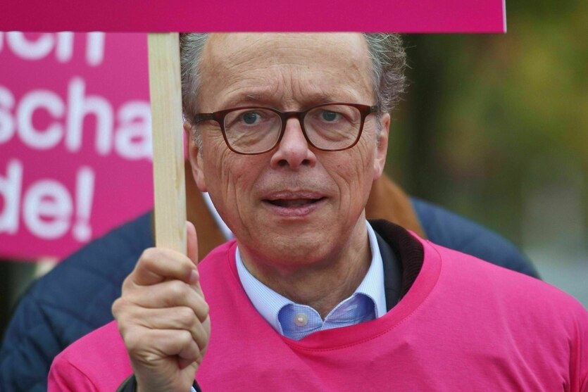 Ein Mann mit Brille und pinkem Pulli (Albrecht von der Hagen) hält ein Schild in die Höhe