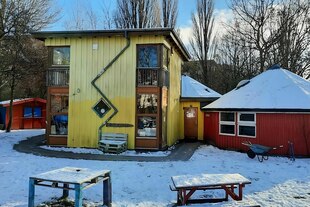 Ein leerer verschneiter Platz mit gelbem Holzhaus mit großen Fenstern und Zickzack-Rinne und roter Jurte