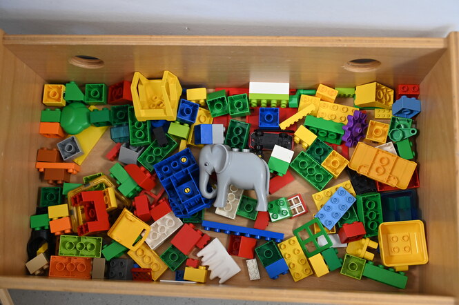 Bunte Lego-Bauklötze liegen in einer Holzbox.