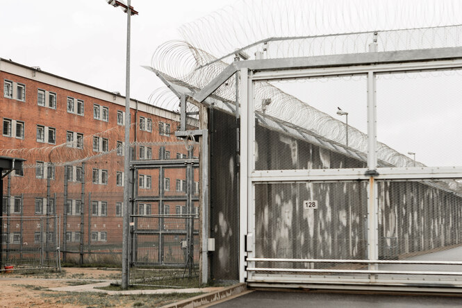 Rotes Backsteingebäude mit vergitterten Fenstern, hohem Zaun und massenhaft Stacheldraht