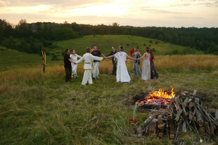 Menschen in altertümlicher russischer Tracht machen in einer Tundralandschaft neben einem Feuer einen Kreistanz