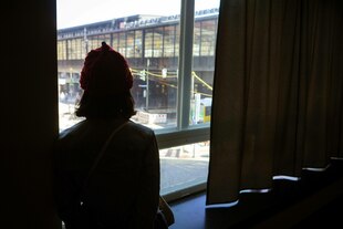 Ein Mensch mit Mütze schaut aus dem Fenster der C/O Galerie auf den Bahnhof Zoo