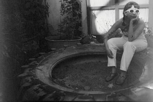 Peki Momés sitzt in einem alten LKW-Reifen und lehnt an einer Hauswand. Sie trägt eine schicke weiße Sonnenbrille