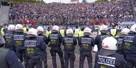 Eine voll besetzte Kurve in einem Fußballstadion, davor Polizisten