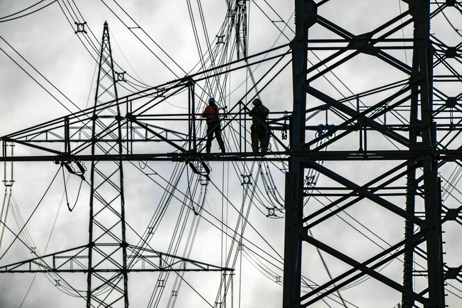 Arbeiter stehen auf den Auslegern eines Hochspannungsmastes