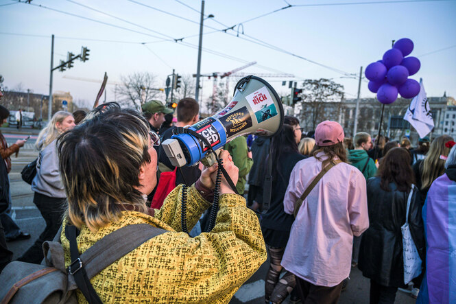 Eine Person mit Megaphon in einer demonstriernden Menschenmenge, lila Luftballons