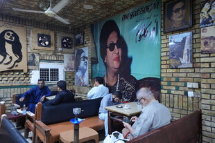 Männer sitzen in einem Café, an der Wand ein riesiges Bild von Um Kulthum mit großer schwarzer Sonnenbrille Männer sitzen in einem Café, an der Wand ein riesiges Bild von Um Kulthum mit großer schwarzer Sonnenbrille