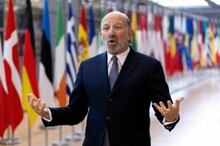 Ein Mann steht vor verschiedenen Flaggen und gestikuliert