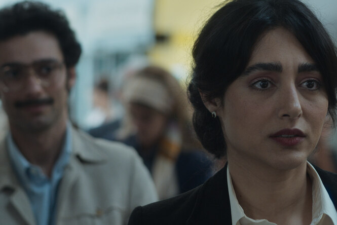 Die Schaupielerin Golshifteh Farahani im Vordergrund, roter Lippenstift, dunkle Haare, bei der Einreise am Flugahfen. Dahinter Darsteller Marandi, Jackett, Brille