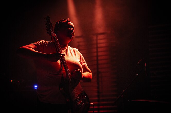 Eine Musikerin der Band Divide & Dissolve mit einer Elektrogitarre im Bühnenlicht