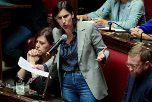 Ein Frau im Blazer (Elly Schlein) gestikulierend am Mikrofon stehend im Parlament