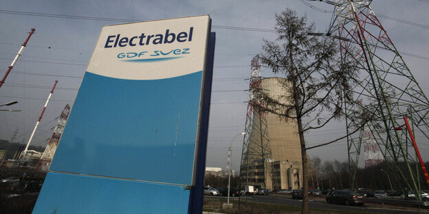 Hinter einem großen blau-weißen Firmenschild mit der Aufschrft Electrabel ist der Kühlturm eines Atomkraftwerks zu sehen