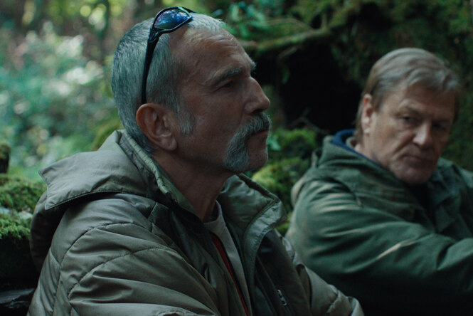 Daniel Day-Lewis und Sean Bean sitzen in einem stark bemoosten Wald.
