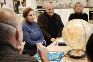 Verschiedene Personen sitzen an einem Tisch, auf dem ein Globus steht