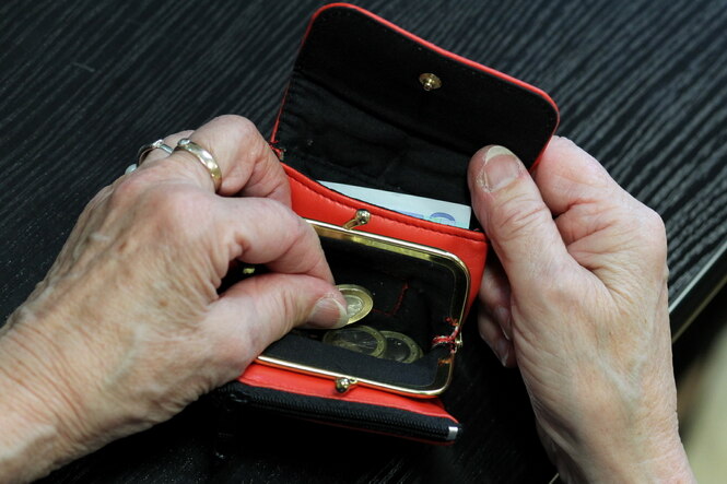 Eine Person hält eine geöffnete Geldbörse mit wenig Geld in der Hand
