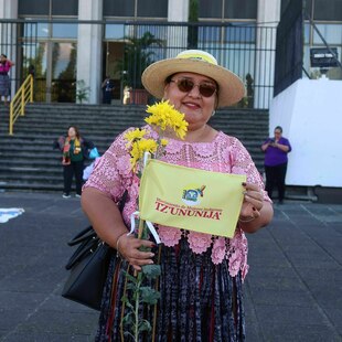 Eine Protestierende hält eine Schild und eine Blume in ihren Händen