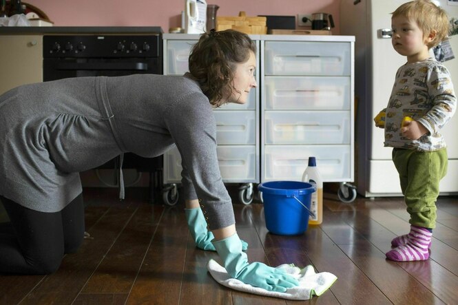Eine Frau putzt den Boden, ein Kleinkind schaut zu