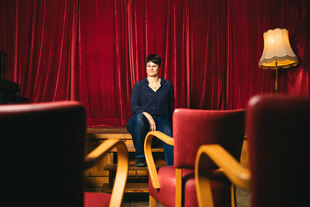Helene Morgenstern sitzt vor einem roten Samtvorhang auf einem Bühnenrand