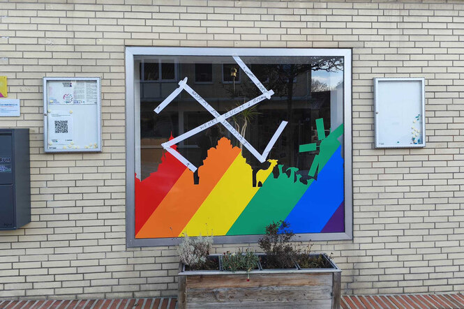 ein Hakenkreuz aus Klebestreifen über einer Stadtsilhouette in Regenbogenfarben