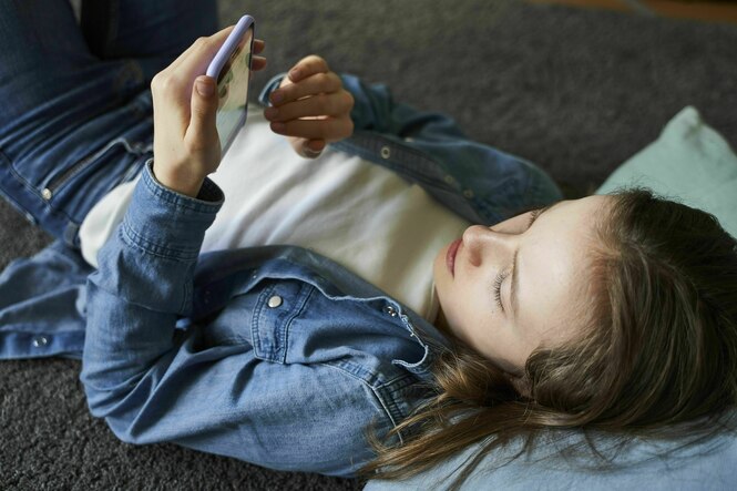 Ein Mädchen liegt auf dem Boden und schaut auf ihr Smartphone