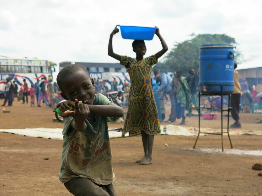 Ein Junge macht Faxen und lacht, ein Mädchen trägt eine blaue Wanne auf ihrem Kopf