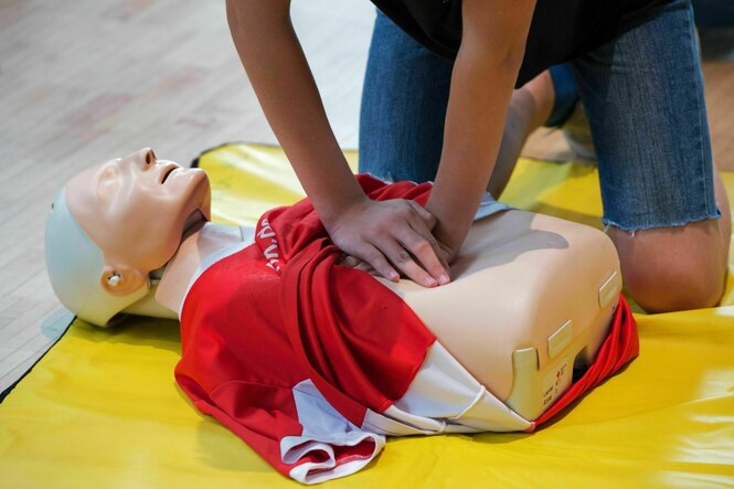 Eine Puppe an der eine Herzdruckmassage trainiert wird -ein Junge drückt auf den Brustkorb der Puppe