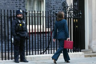 Eine Frau läuft mit einem roten Koffer in der Hand an einem Polizisten vorbei