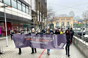 Menschen demonstrieren vor Hannovers Hauptbahnhof mit einem violetten Banner, auf dem steht: 