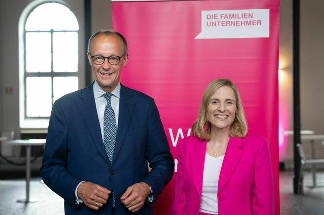 Friedrich Merz und Marie-Christine Ostermann,beide gut gelaunt vor einem Transparent des Verbands "Die Familienunternehmer"