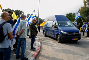 Menschen stehen mit israelischen Flaggen an einer Straße, auf der ein Transporter fährt.