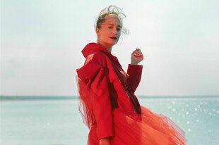 Eine Frau in rotem Tüllkleid steht auf einem Stein auf dem Wasser